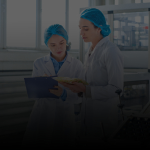 Image of two people in white coats and hair bonnets taking notes