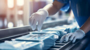 Hands of a worker placing packaged medical equipment into boxes on a conveyor belt, part of the healthcare supply chain